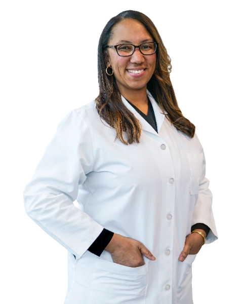 Professional headshot of Dr. Tamara Green wearing a white lab coat over dark scrubs and glasses, smiling confidently against a black background. This official clinical portrait represents a healthcare provider ready for patient consultations and medical practice.